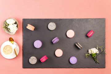 French macarons or macaroons, and incarnation white flower on a slate, with coffee and white incarnations flowers in a bowl.