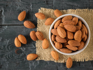 Almonds in a white bowl on a piece of burlap on a wooden table. Vegetarian food. Flat lay.