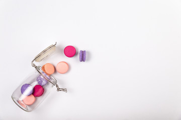 French pink, fuchsia and purple macarons or macaroons, falling out of a glass jar over a white background with large copyspace.