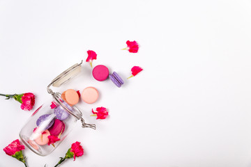 French pink, fuchsia and purple macarons or macaroons, with fuchsia incarnation flowers and petals falling out of a glass jar over a white background with large copyspace.