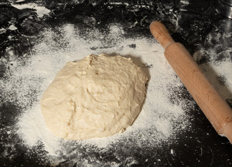 On the black Desk a pile of dough with a rolling pin sprinkled with flour. Horizontal photo format