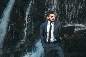 Man with notebook stand near waterfall. Modern technology. Successful businessman follow flow. Guy...