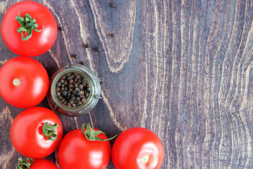 Red ripe tomatoes and black pepper on a brown wooden background. Top view. Copy space.