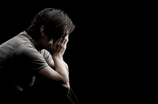 Man sitting alone felling sad worry regret or fear and hand off his face on dark black background