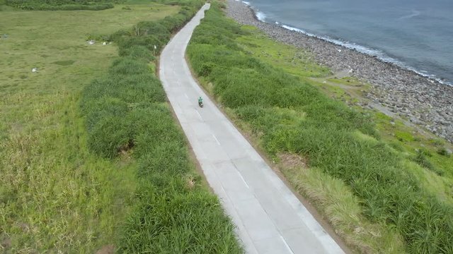 A drone follow clip of a man riding a scooter on the hills of Batanes.