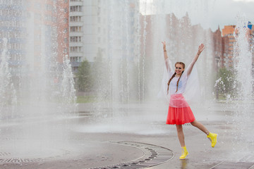 Young wet pretty girl with two braids in yellow boots stands near fountain.