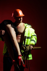 Having a strong sexual appeal in constructor uniform. Muscular man in worker uniform holding sexy woman. Handsome man dressed like constructor or miner, uniform fetish. Uniform fetishism