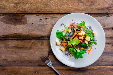 Salad of fresh vegetables in a white dish placed on an old wooden table.top view.