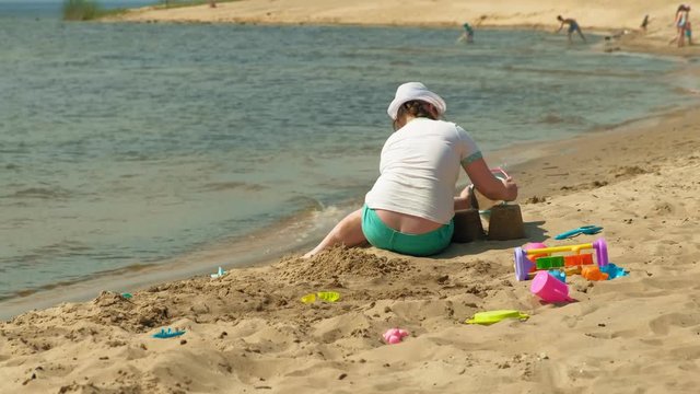  Girl builds a sand castle on the river bank