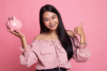 Asian woman thumbs up with pig coin bank.