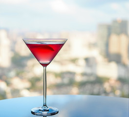 Red martini cocktail on glass table with cityscape as background in sunny day