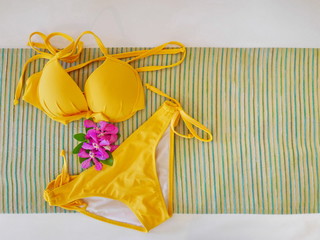 top view of yellow bikini with purple orchid on abstract fabric,copy space.teenage colorful swiming suit