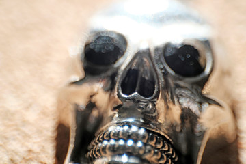 Metal skull on light background. Bright, shiny keychain close-up in sunlight.
