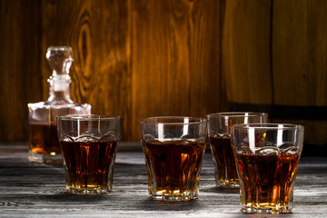 strong alcoholic drinks in glasses, cognac and brandy in decanters stand on an oak barrel