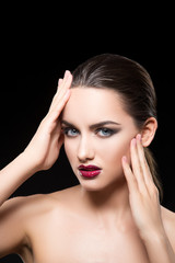 Fototapeta na wymiar Attractive beautiful young adult woman studio portrait, glossy red lips make-up, smoky eyes, hands touching face perfect skin. Copy space. Black background