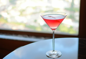 Red cocktail in martini glass with sunny cityscape as background