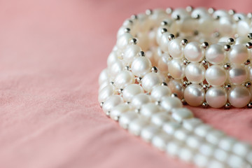 Beautiful white pearl necklace on a coral color textile background close up