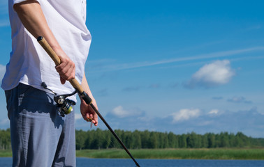 close-up, a man's hand, holds a fishing rod and fishes, against the backdrop of the lake