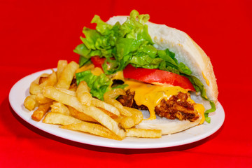 Sandwiches fried chicken, tomatoes, lettuce leaves and French fries with red background.