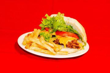 Sandwiches fried chicken, tomatoes, lettuce leaves and French fries with red background.