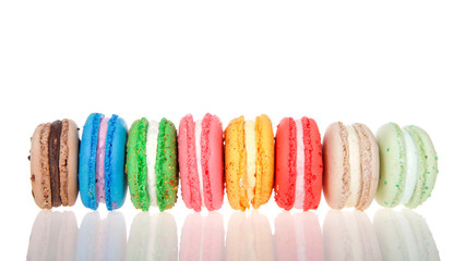 Row of macaron cookies laying sideways side by side multiple colors and flavors on a reflective surface isolated on white. Traditional french treat.