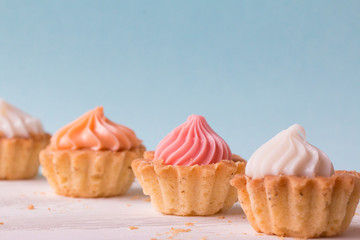 Small cakes and with cream on a white table on a blue background . Selective focus. 