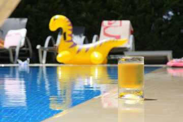  Transparent glass cup with lemonade or juice near the pool in the hot summer. Vacation. Pool. Cold drink.