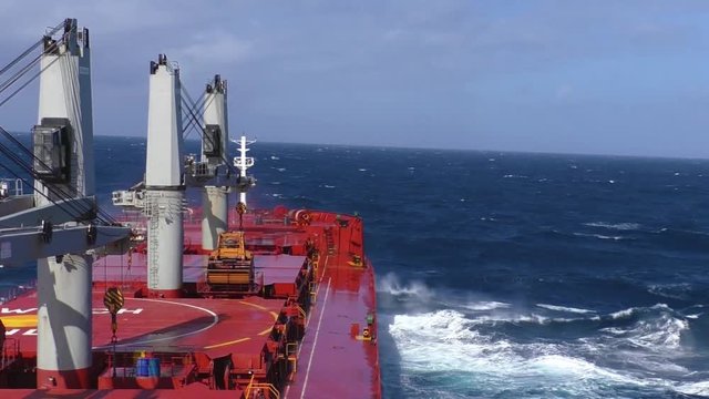 Cargo ship in stormy sea. View from navigation bridge to a large wave crashing into bow of bulk carrier in the stormy sea.