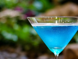 Blue cocktail in martini glass with green garden plants as background