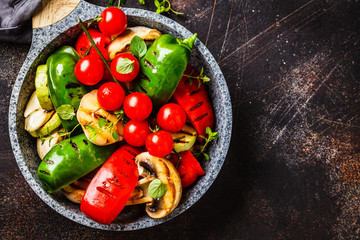 Grilled vegetables (peppers, zucchini, mushrooms and tomatoes in pan, dark background.