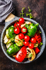 Grilled vegetables (peppers, zucchini, mushrooms and tomatoes in pan, dark background.