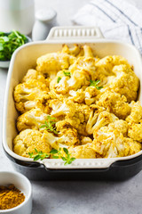 Baked cauliflower in oven dish on white concrete background.