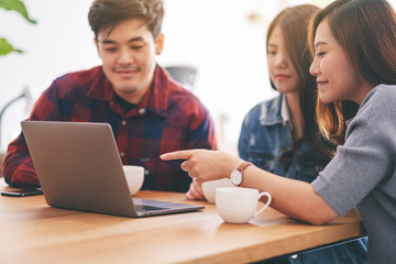 Fototapeta premium Three young asian people using and looking at the same laptop computer during a meeting