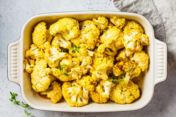 Baked cauliflower in oven dish on white concrete background.