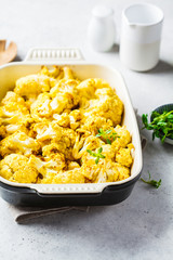 Baked cauliflower in oven dish on white concrete background.