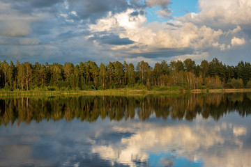 beautiful sunset by the lake with green grass meadow and white clouds in the blue sky