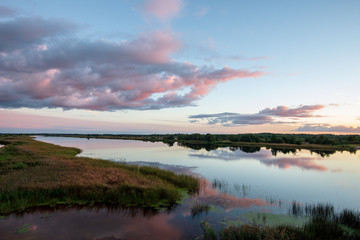beautiful sunset by the lake with green grass meadow and white clouds in the blue sky