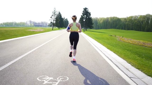 Woman runner run on empty road. Morning time. Slow motion, back view