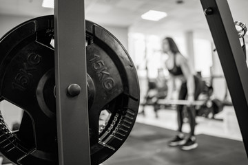 Iron barbell disk on the background of a woman training in the gym. Fifteen kg on the barbell disk. Close-up. Black and white photo.