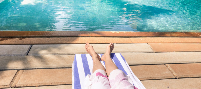 Bare feet of young lady lying on deck chair sunbathing by the swimming pool.