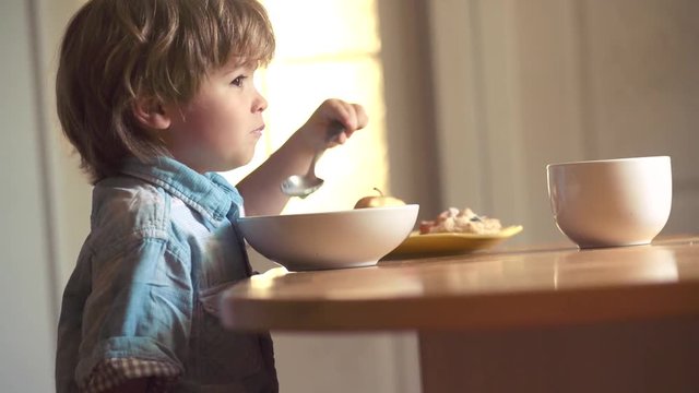 Portrait of beautiful child having breakfast at home. The child in the kitchen at the table eating. Laughing cute child baby boy sitting in highchair and eating on kitchen background.