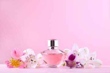 Bottle of perfume with flowers on pink background
