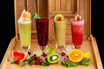 Group of fresh healthy fruit smoothies at wooden table background with ingredients around.