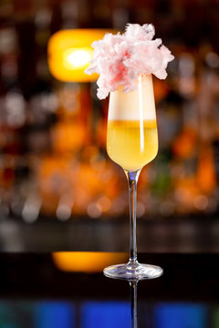 Closeup vertical glass of yellow layered cocktail decorated with cotton candy at bar counter background.
