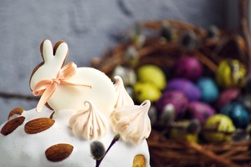 Obraz na płótnie Canvas Easter cake in the form of a rabbit on a tree cut, a table decorated with rabbits and multi-colored quail eggs. against the background of the basket with willow, close-up