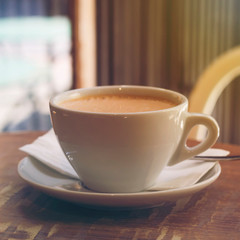 Cup of cappuccino coffee or orange thai tea on the brown wooden table in street cafe with sunlight highlight, toned. Close-up, copy space, square format