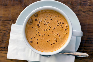 Cup of cappuccino coffee or orange thai tea, plate, spoon, napkin on the brown wooden table in cafe. Close-up, top view, flat lay, copy space