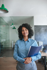 Smiling young businesswoman standing in an office carrying files