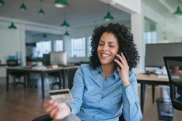 Fototapeta premium Smiling businesswoman ordering something using her cellphone and credit card 