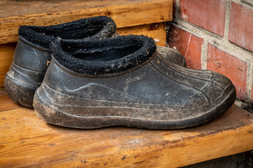 A pair of dirty old black rubber boots (galoshes) on the threshold of the house. Close up.